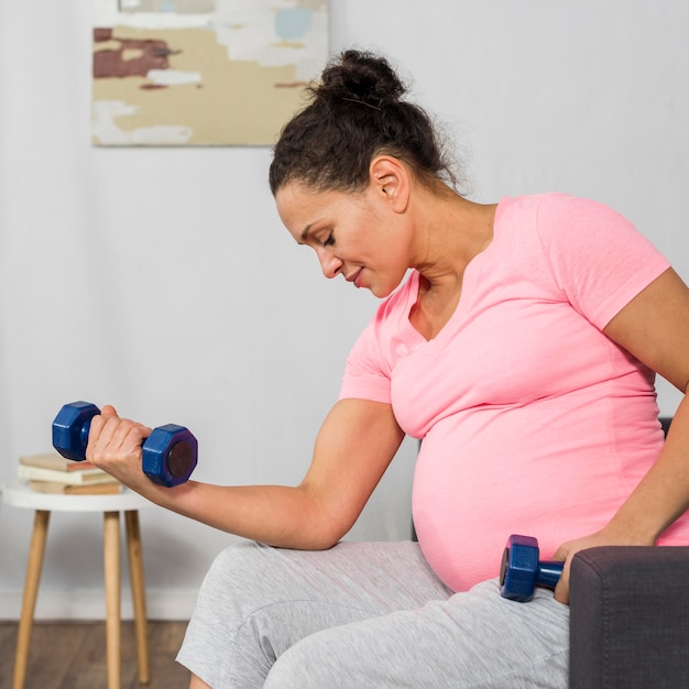 Foto gratuita vista lateral de la mujer embarazada en casa haciendo ejercicio con pesas