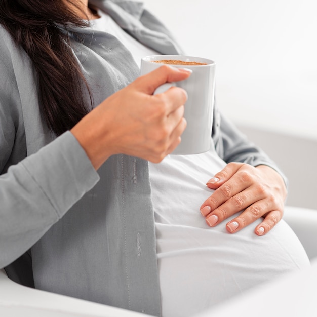 Vista lateral de la mujer embarazada en casa sosteniendo una taza de café