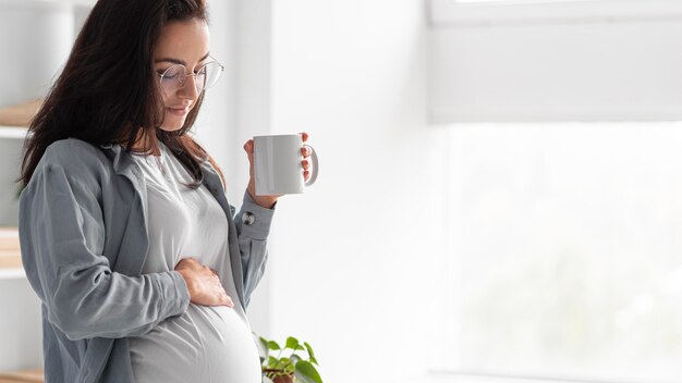 Vista lateral de la mujer embarazada en casa con taza de café