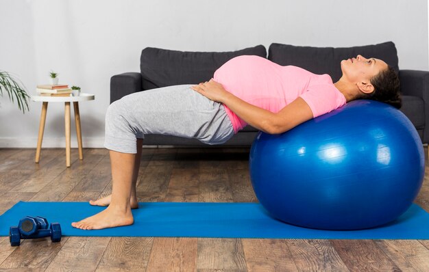 Vista lateral de la mujer embarazada con pelota para hacer ejercicio en casa