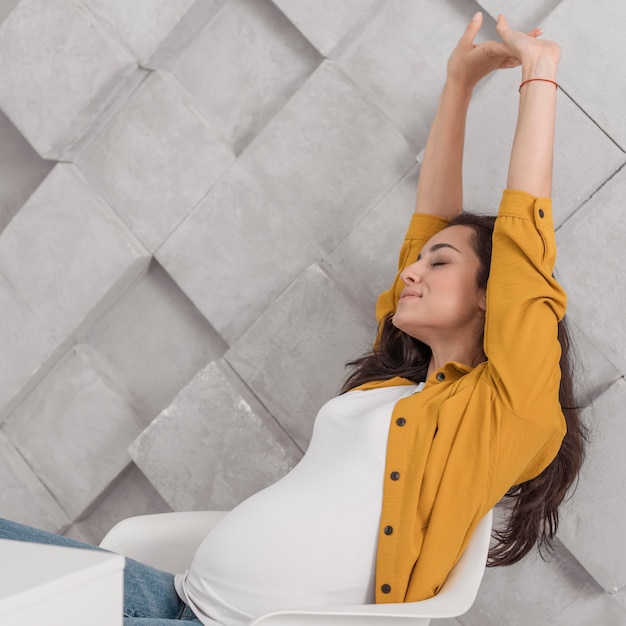 Vista lateral de la mujer embarazada que se extiende mientras está en una silla en casa