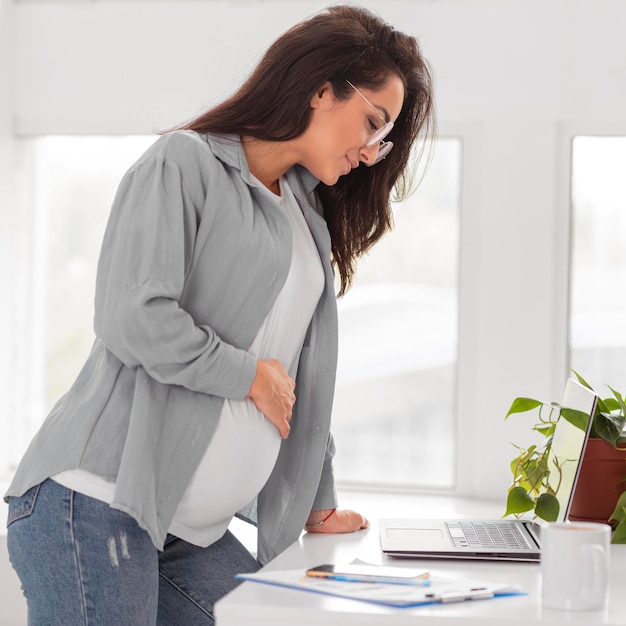 Vista lateral de la mujer embarazada que trabaja en la computadora portátil en casa