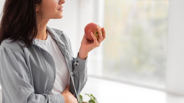 Vista lateral de la mujer embarazada sosteniendo una manzana con espacio de copia