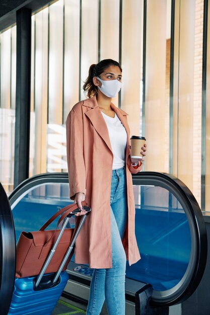 Vista lateral de la mujer con equipaje y máscara médica durante la pandemia en el aeropuerto