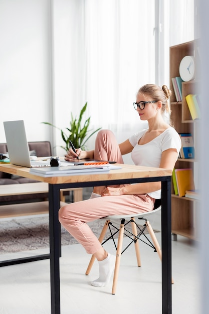 Vista lateral de la mujer en el escritorio trabajando mientras está en casa