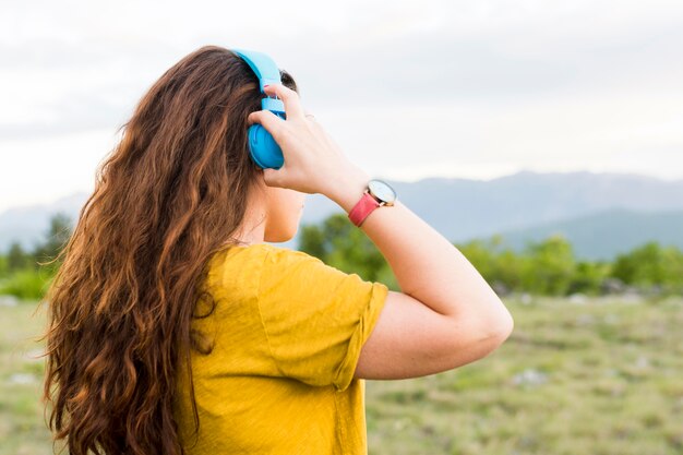 Vista lateral de la mujer escuchando música con auriculares en la naturaleza