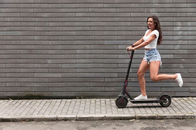 Vista lateral de la mujer feliz montando un scooter eléctrico