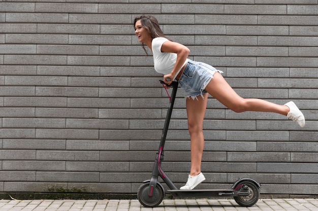 Vista lateral de la mujer feliz posando en scooter eléctrico