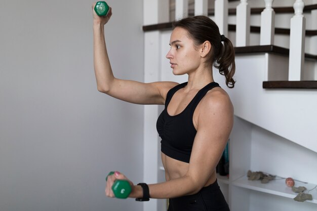 Vista lateral de la mujer flexionando los brazos mientras hace ejercicio con pesas