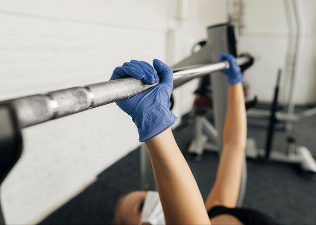 Vista lateral de la mujer con guantes y máscara médica trabajando en el gimnasio