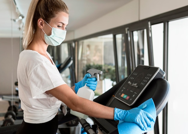 Foto gratuita vista lateral de la mujer con guantes y solución de limpieza desinfectando equipos de gimnasio