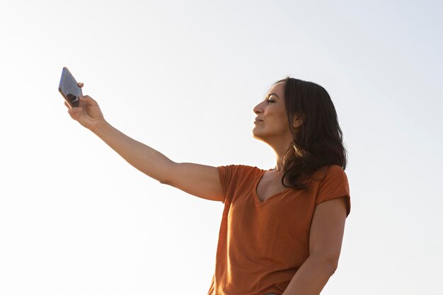 Vista lateral de la mujer hablando selfie al aire libre