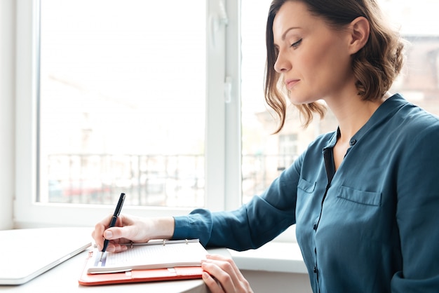 Vista lateral de una mujer haciendo notas en su diario