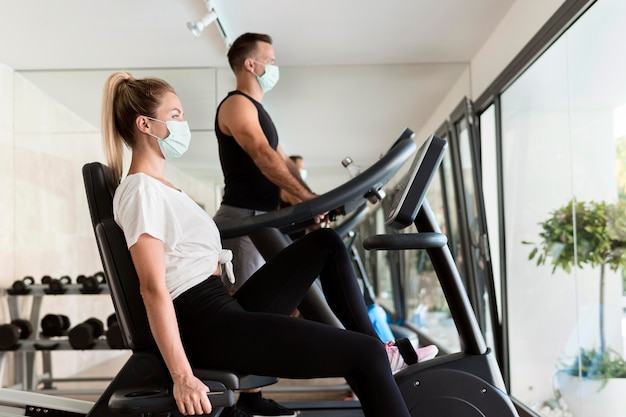 Vista lateral de la mujer y el hombre en el gimnasio con máscaras médicas