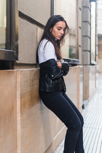 Foto gratuita vista lateral de una mujer joven apoyada en la pared junto a la acera