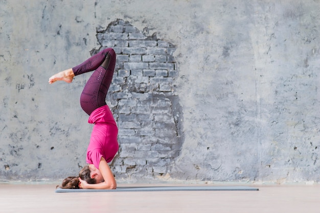 Vista lateral de una mujer joven de la aptitud que se coloca en su cabeza que hace yoga