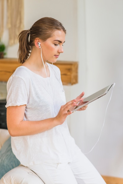 Vista lateral de la mujer joven con el auricular que navega la tableta digital
