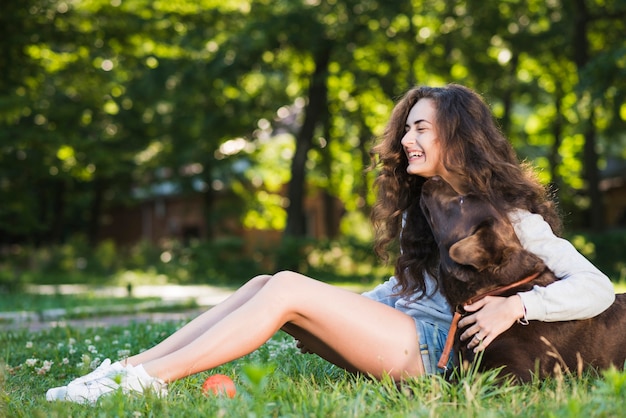 Vista lateral de una mujer joven feliz sentada con su perro en el jardín