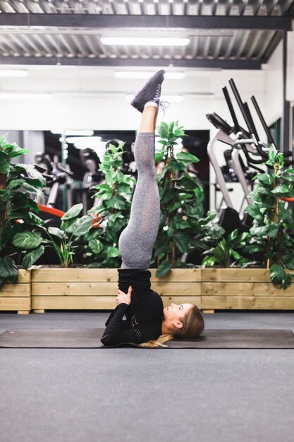 Vista lateral de una mujer joven haciendo ejercicio pierna arriba en la estera de yoga