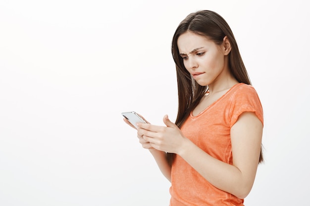 Vista lateral de una mujer joven preocupada y confundida mirando el teléfono inteligente en cuestión