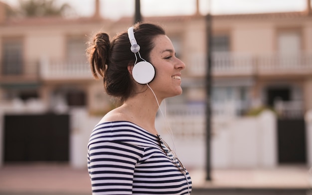 Vista lateral de una mujer joven que disfruta de la música que escucha en el auricular