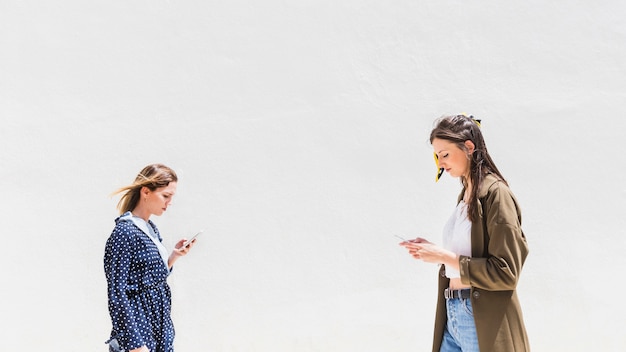 Vista lateral de la mujer joven que usa smartphone contra el contexto blanco