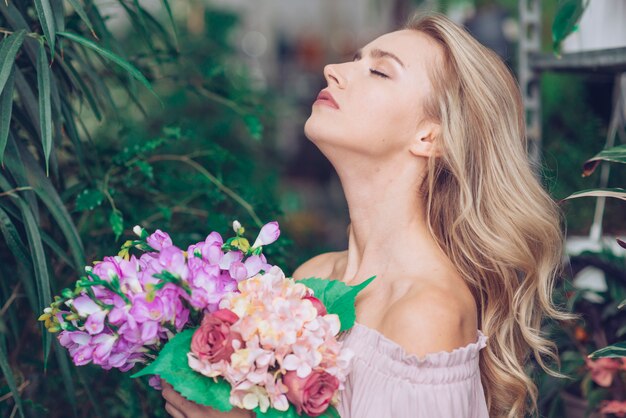 Vista lateral de una mujer joven relajada que se coloca en el jardín que sostiene el ramo colorido de la flor