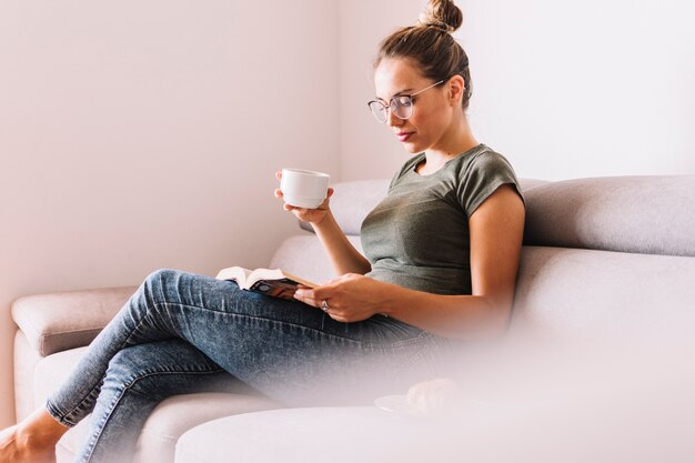 Vista lateral, de, un, mujer joven, sentado, en, sofá, libro de lectura