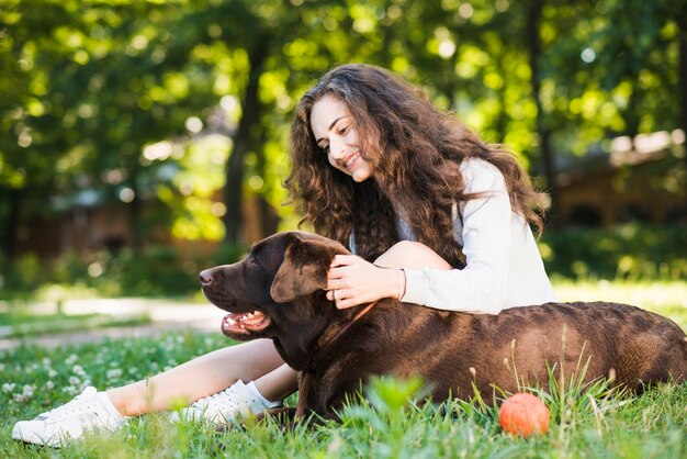 Vista lateral de una mujer joven sonriente acariciando a su perro en el jardín