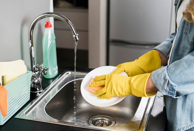 Vista lateral de la mujer lavando un plato en el fregadero