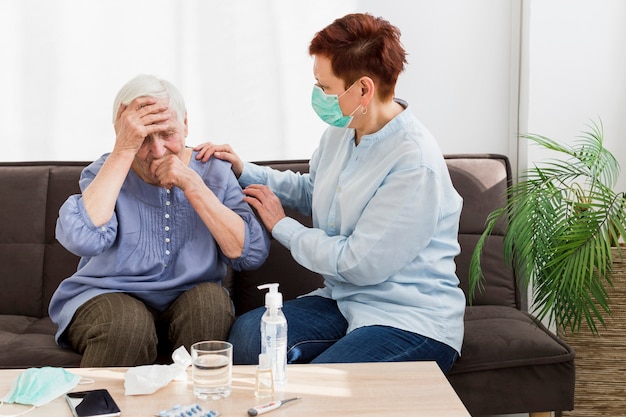 Vista lateral de la mujer con máscara médica cuidando a una anciana en casa