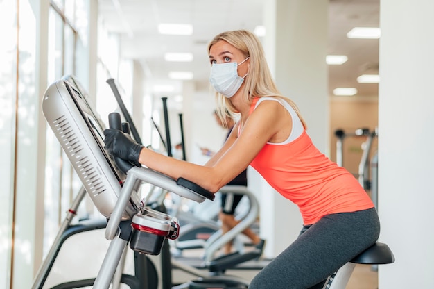 Vista lateral de la mujer con máscara médica y guantes trabajando en el gimnasio