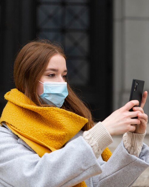 Vista lateral de la mujer con máscara médica tomando fotografías con smartphone