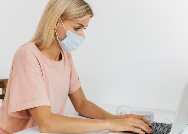 Vista lateral de la mujer con máscara médica trabajando desde casa durante la pandemia