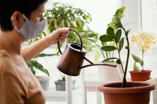 Vista lateral de la mujer con mascarilla con regadera para planta de interior