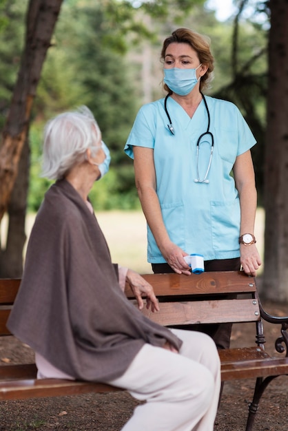 Vista lateral de la mujer mayor con máscara médica en el hogar de ancianos con enfermera