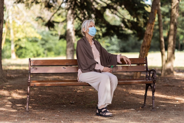 Foto gratuita vista lateral de la mujer mayor con máscara médica sentado en un banco al aire libre en un hogar de ancianos