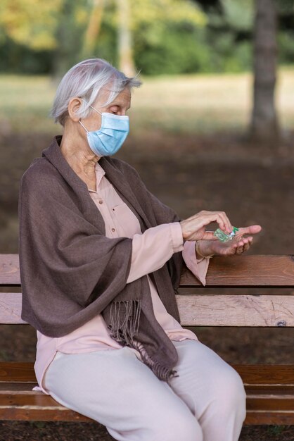 Vista lateral de la mujer mayor con mascarilla médica y desinfectante de manos