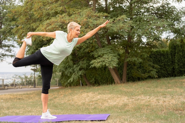 Vista lateral de la mujer mayor practicando yoga al aire libre en el parque
