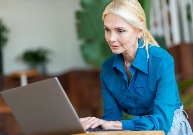 Vista lateral de la mujer mayor que trabaja en la computadora portátil mientras está fuera