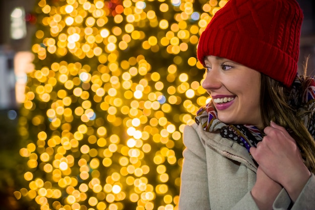 Vista lateral mujer en el mercado festivo de Navidad por la noche Mujer feliz mirando hacia arriba con la luz de Navidad en la noche