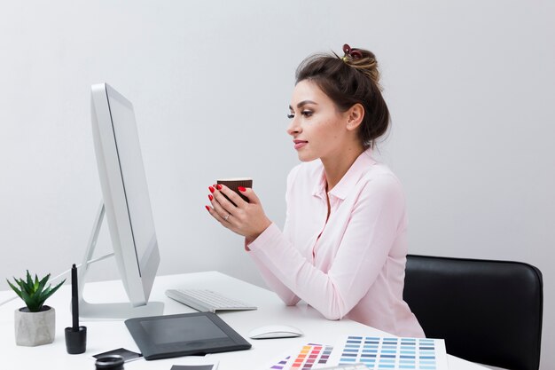 Vista lateral de la mujer mirando la computadora mientras sostiene la taza de café