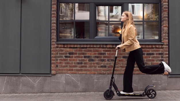 Vista lateral de la mujer montando scooter eléctrico al aire libre con espacio de copia