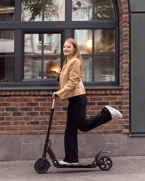 Vista lateral de la mujer montando scooter eléctrico al aire libre