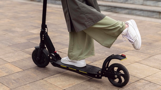 Vista lateral de la mujer montando su scooter eléctrico al aire libre