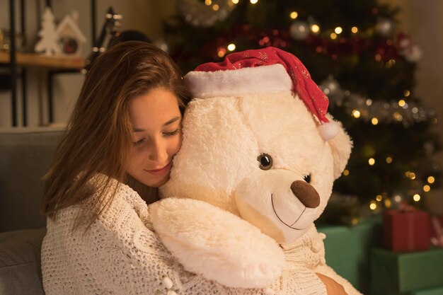 Vista lateral de la mujer mujer en navidad abrazando a su osito de peluche