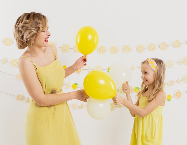 Vista lateral de la mujer y la niña posando con globos y sonriendo