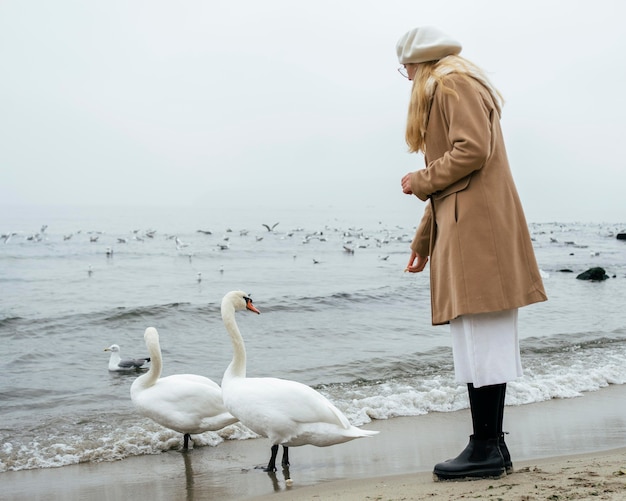 Foto gratuita vista lateral de la mujer en la playa en invierno con cisnes