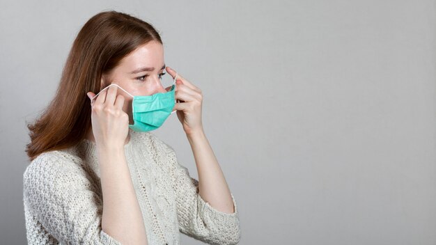 Vista lateral de la mujer poniéndose mascarilla médica con espacio de copia