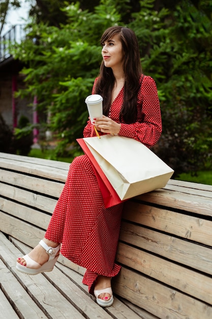 Vista lateral de la mujer posando afuera con bolsas de la compra y una taza de café